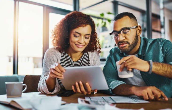 This image shows a couple reviewing their financial records while enjoying coffee. This practice promotes holistic financial well-being through financial behavior change.