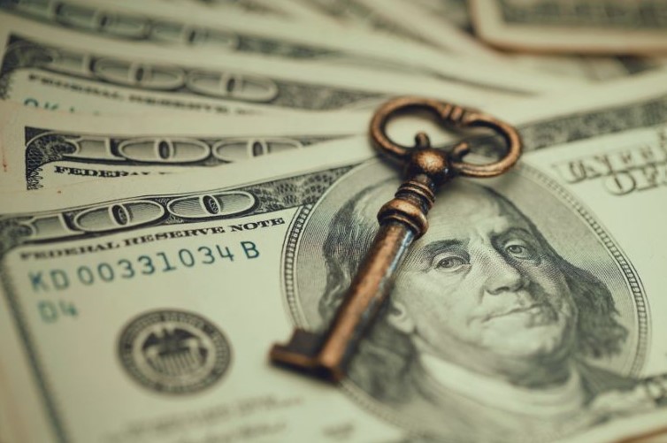 This image shows a key on top of $100 USD bills. holistic, suggesting that changing financial behavior change is a key to financial well-being
